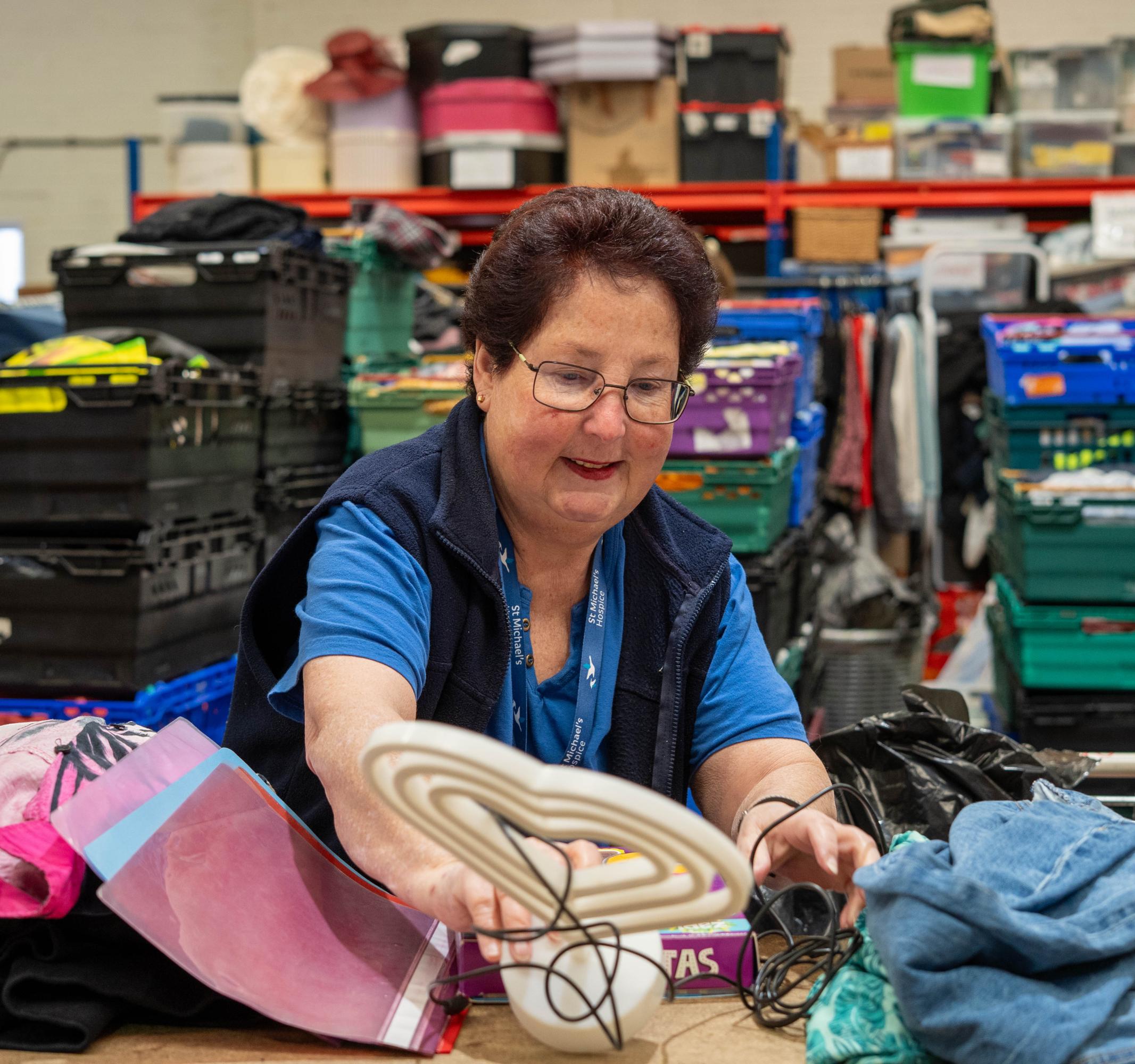 Woman in blue shirt sorting shoes and clothes in a busy warehouse setting.