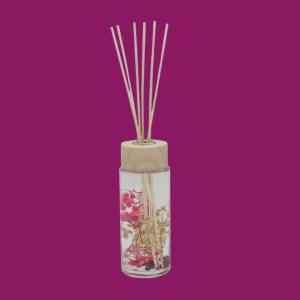 Reed diffuser with clear glass bottle, wooden cap, and dried red and gold botanicals.