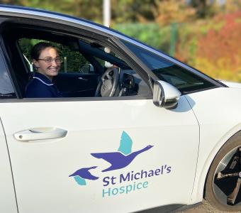 Smiling woman in uniform in a white St Michael's Hospice car.