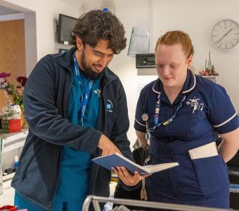 Healthcare workers, a man and woman, reviewing a patient chart together.