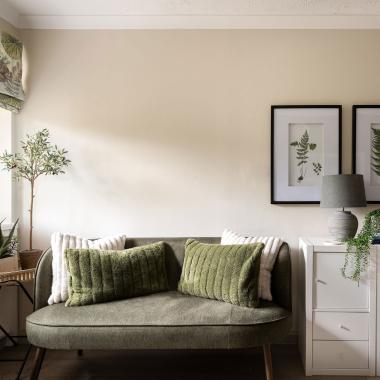 Bright living room with an olive green sofa, framed botanical prints, and a tall potted plant.