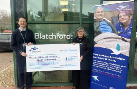 Man and woman hold a large check for St. Michael's Hospice outside Blatchford building.