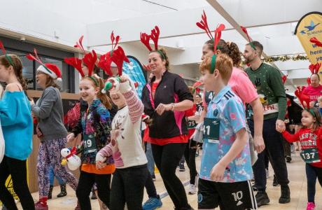 Adults and children in Christmas outfits, some with reindeer antlers, at a festive indoor event.