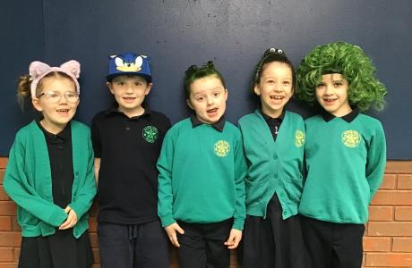 Five smiling children in green school uniform, some wearing wigs or hats.
