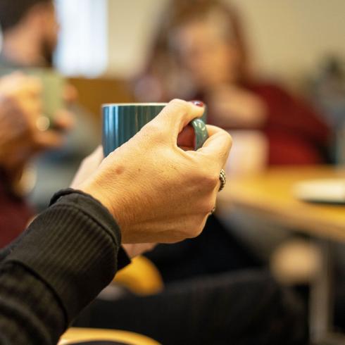 Close-up of hands holding a teal mug, blurred people in the background.