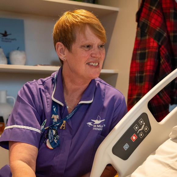 Friendly nurse in purple uniform talks to a patient in a hospital bed.