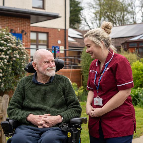 Smiling man in wheelchair talks with a smiling nurse in a garden.