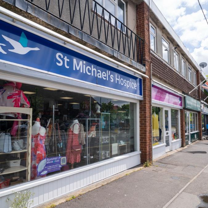St Michael's Hospice charity shop with blue sign and other stores on a street.