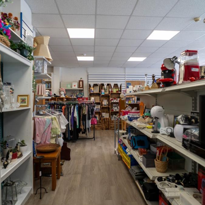 Interior of a brightly lit thrift store with shelves full of clothes and various household items.