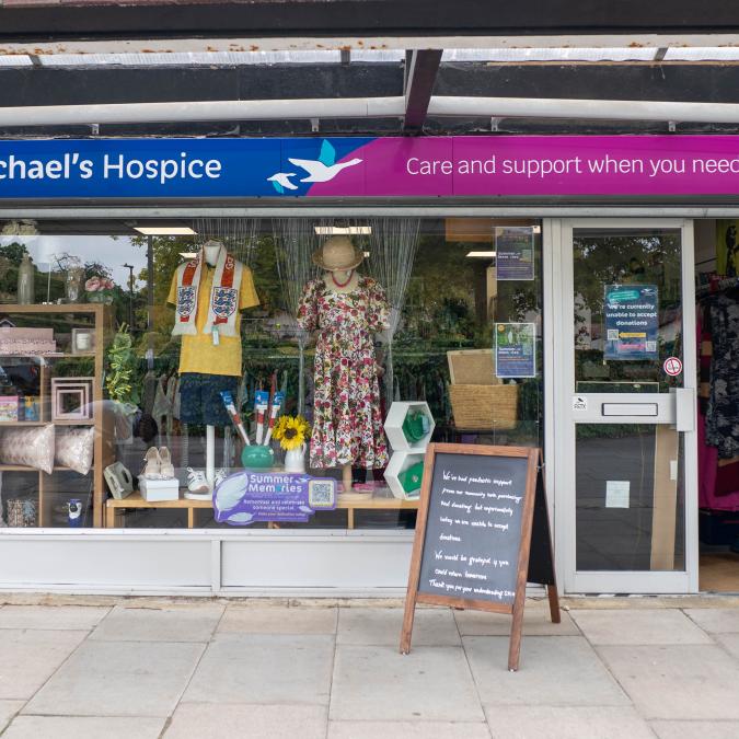 St Michael's Hospice Kempshott charity shop storefront with displayed clothing and goods.