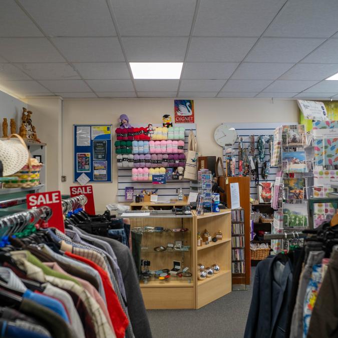 Interior of a small shop with clothing racks and a counter displaying various items.