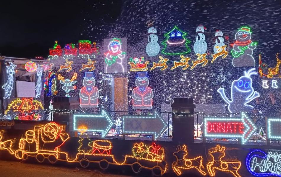 Colorful Christmas light display at night with Santa, reindeer, snowmen, and falling snow.