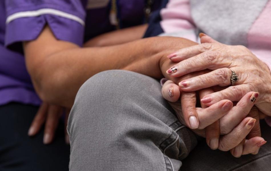 Caregiver's hand gently holding an older person's wrinkled hand.