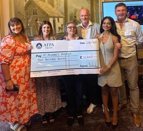 Six smiling people hold a giant check for £10,000 donated to St. Michael's Hospice.