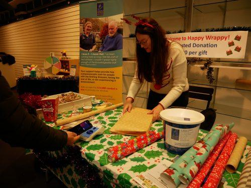 Woman in reindeer antlers wraps a present at a festive "Happy Wrappy" station.