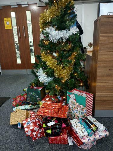 Christmas tree decorated with gold and silver tinsel, surrounded by many wrapped gifts.