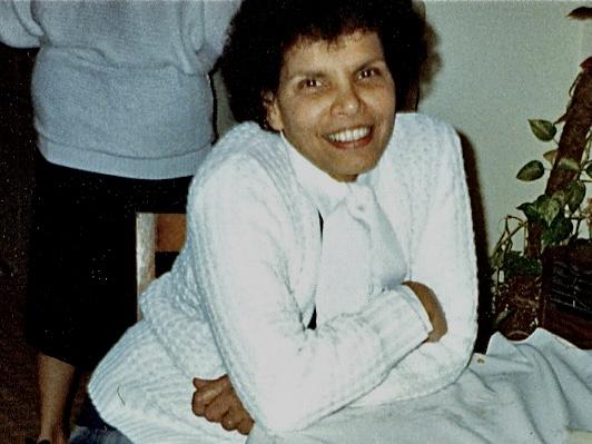 Photograph of a smiling woman with dark curly hair wearing a white knitted sweater.