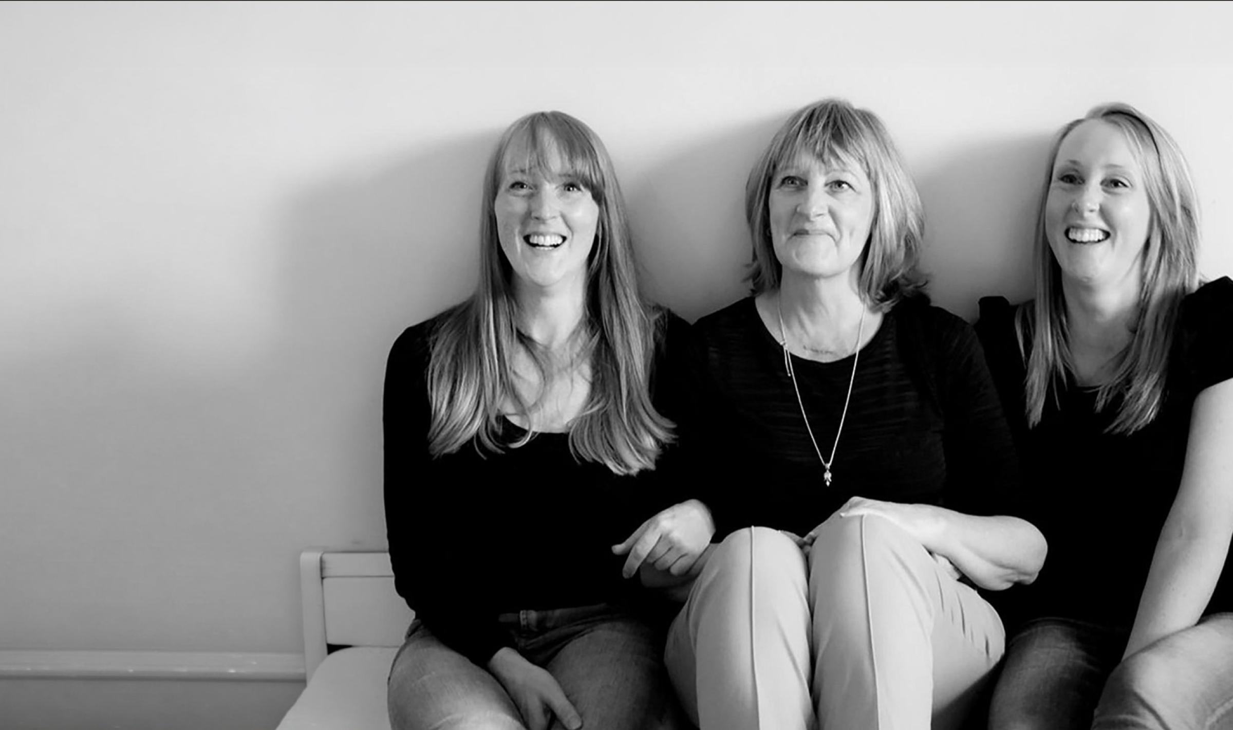 Black and white photo: Three smiling women, one older and two younger, sitting.