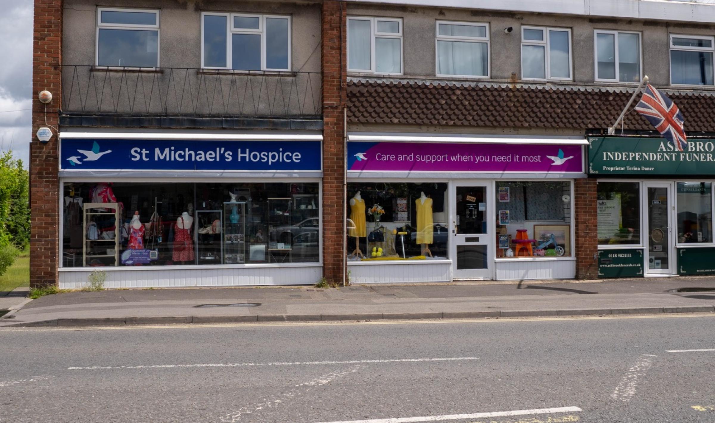 Row of UK charity shops, including St Michael's Hospice, with a Union Jack flag on the right.